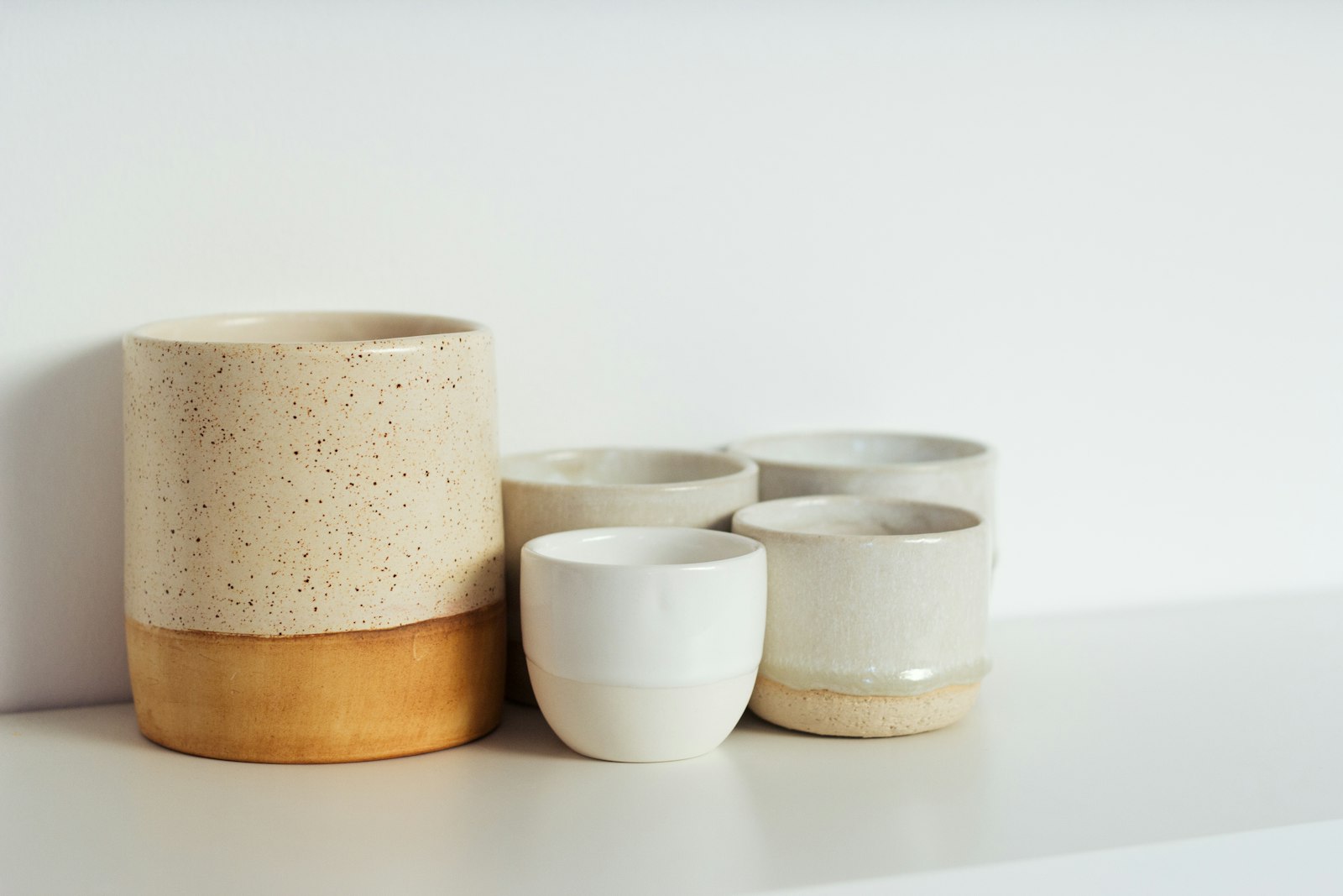Speckled ceramic cups and a two-tone vase arranged on a white shelf. It accompanies an article about FAQ sections that help buyers and search engines.