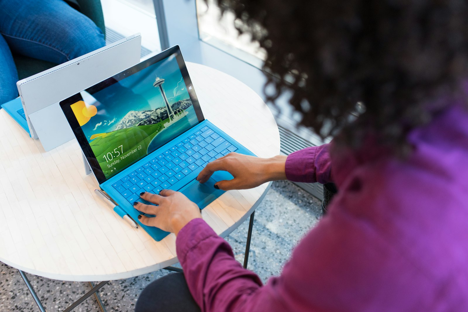 A person in a purple shirt typing on a bright blue laptop at a round table. It accompanies an article about How to brief a studio for a marketing site.