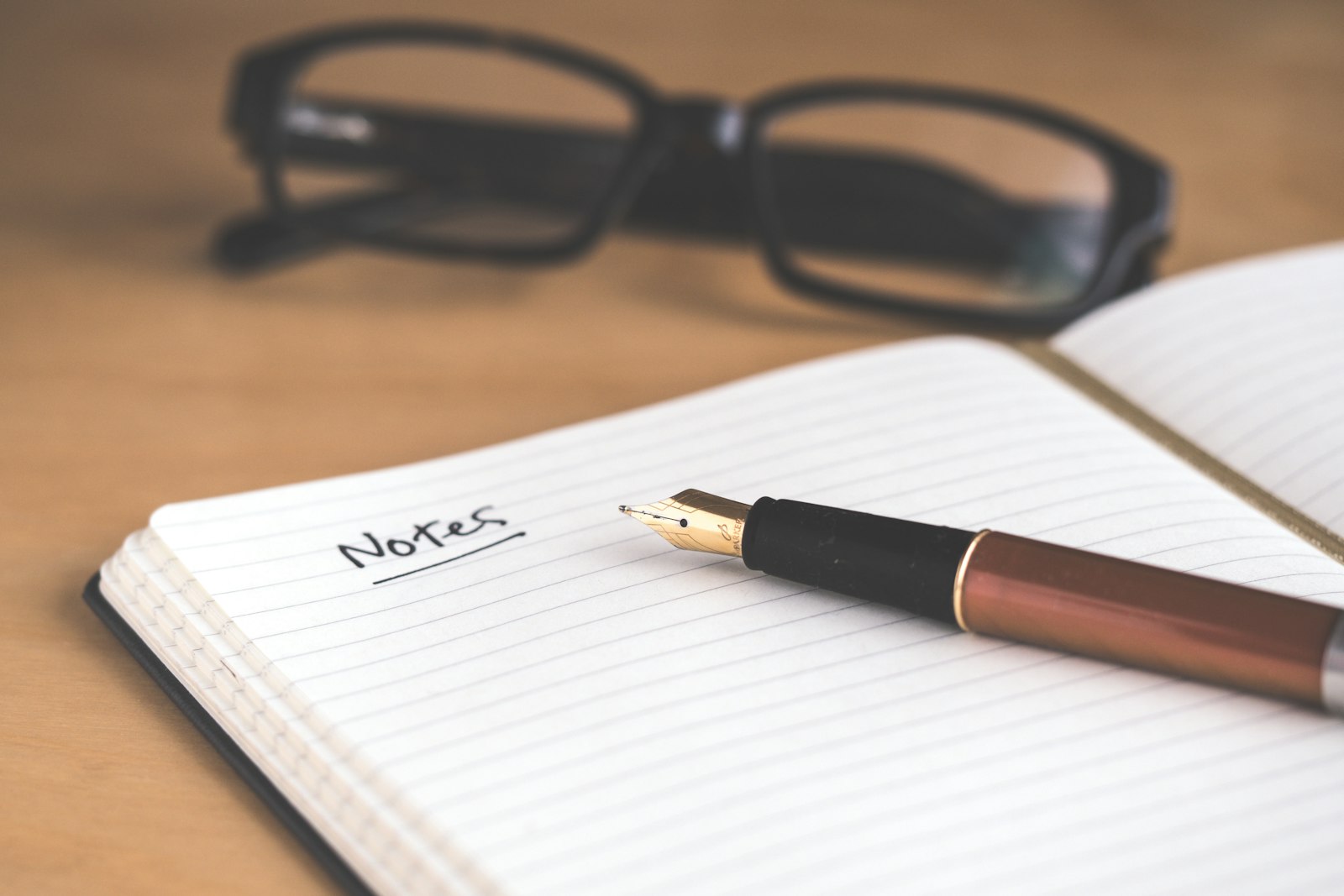 An open notebook with the word Notes underlined, a fountain pen, and glasses on a wooden desk. It accompanies an article about Component libraries that match the brand.