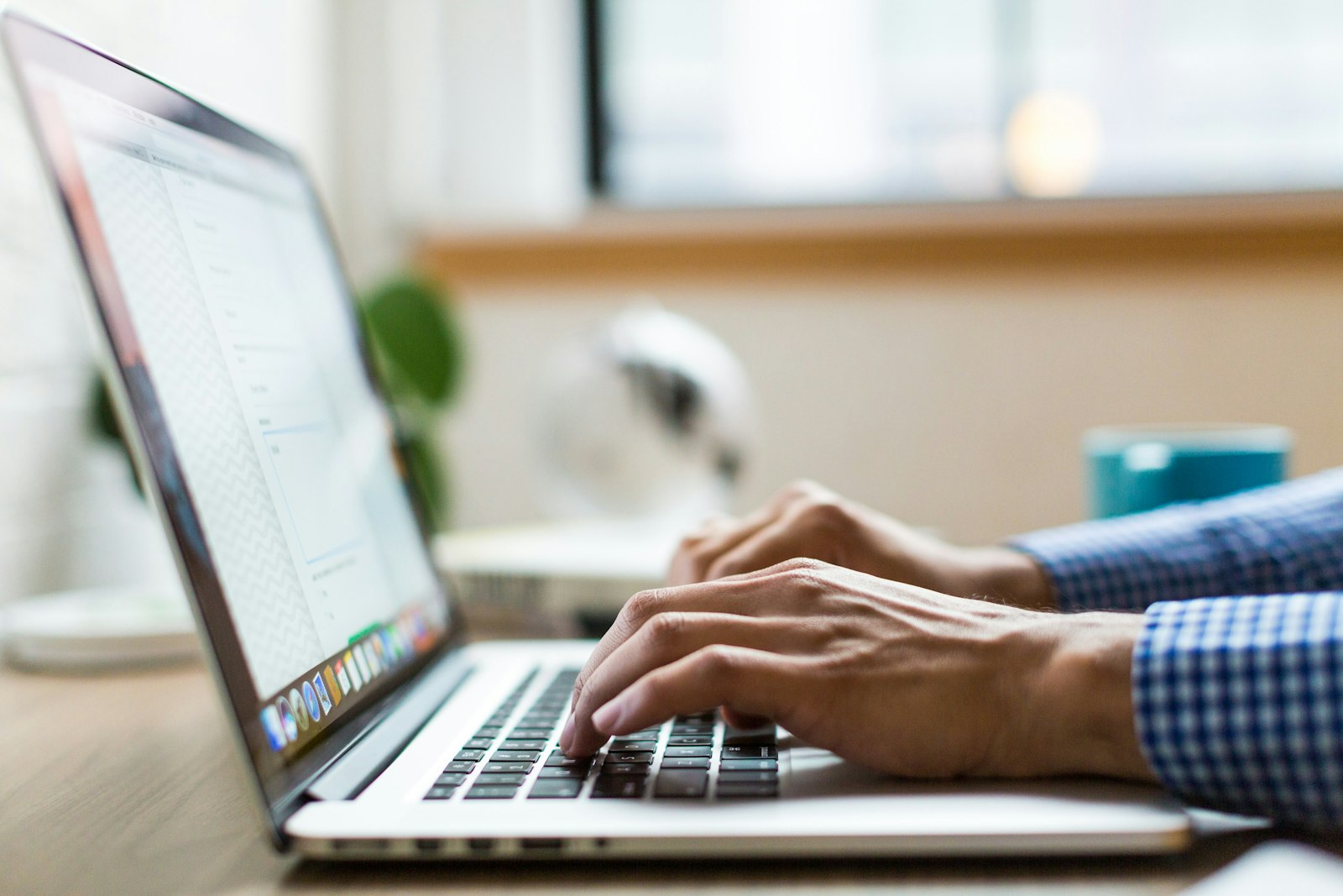 Hands typing on a laptop at a wooden desk near a window. It accompanies an article about What founders should expect from a Next.js company site.