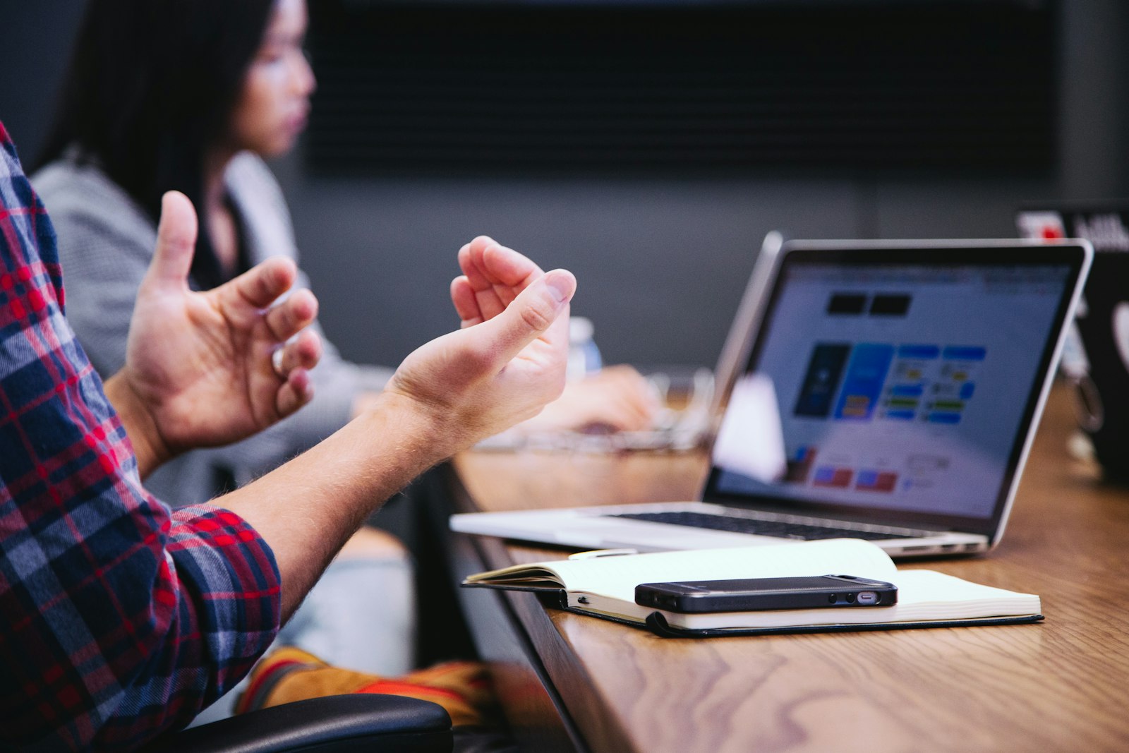 A person gesturing in a meeting, with a laptop showing a colorful layout, a notebook, and a phone on the table. It accompanies an article about How to give design feedback without restarting the project.